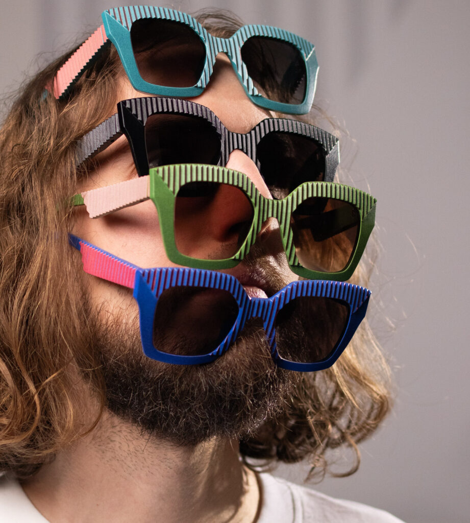 CEHO Studio portrait of a man wearing four stacked, colorful sunglasses from the AVA eyewear collection, highlighting playful, 3D-printed design.