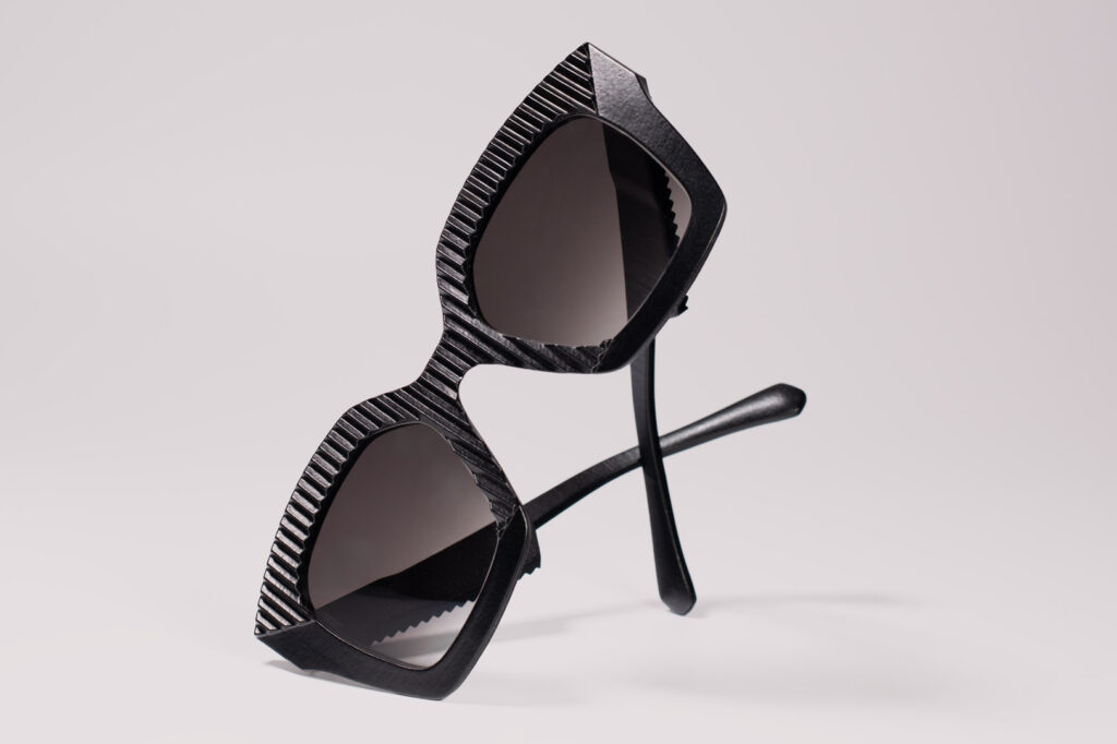 Studio product photo of AVA Black Moon sunglasses by CEHO Studio, featuring bold black frames with ridged vertical stripes, set against a soft neutral background.